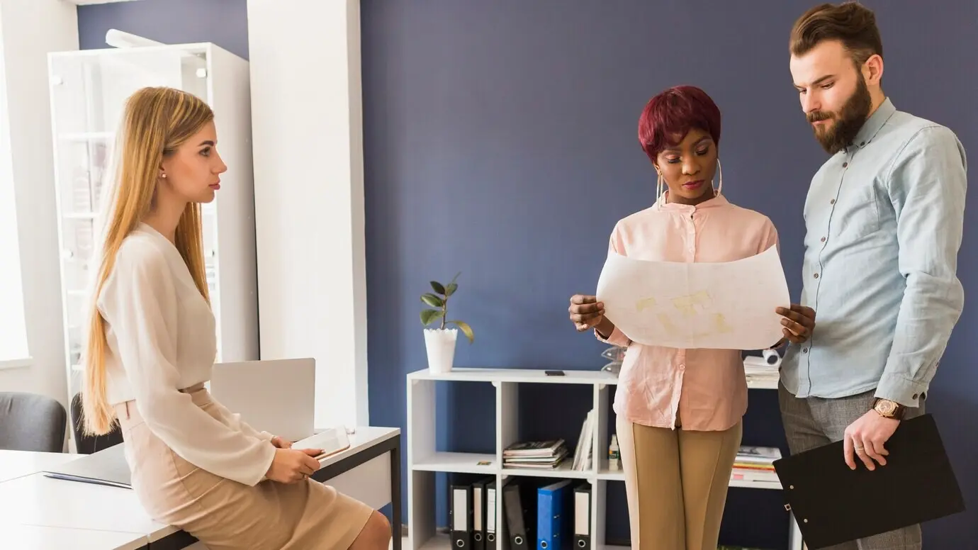 Женщина смотрит на коллег, обсуждающих черновик.